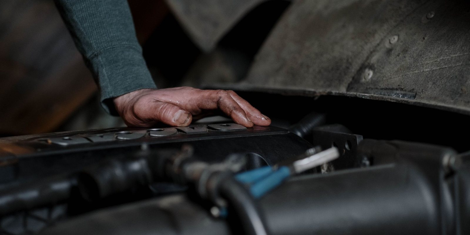 Mão com graxa apoiada sobre a tampa do motor de um carro, com o capô aberto